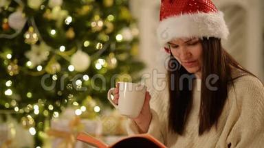 圣诞背景下戴着圣诞帽、<strong>手捧</strong>白杯、<strong>手捧</strong>书的美丽不伦特特写镜头